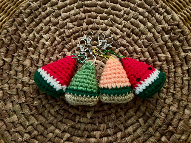 Four crocheted keychains that look like a triangular slice of melon. From left to right they’re made to represent: Watermelon, Honeydew, Cantaloupe, and a watermelon with small safety eyes. 